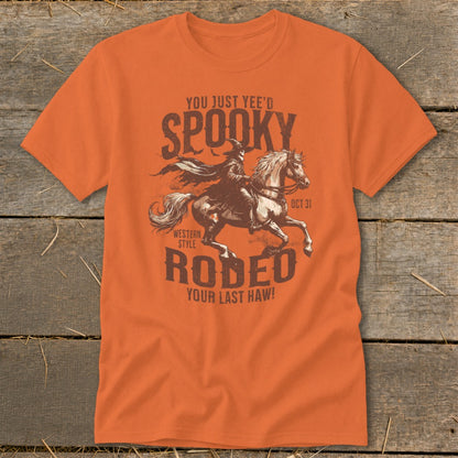 Orange t-shirt with graphic of person in witch hat riding horse with text Spooky Rodeo Oct 31.