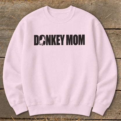 Light pink crewneck sweatshirt featuring black block lettering that reads DONKEY MOM on a rustic wooden surface.
