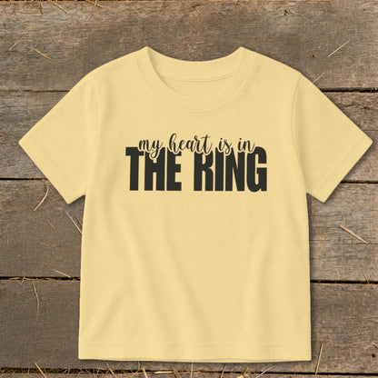 A yellow short-sleeve t-shirt with black text that reads "my heart is in THE RING" centered on the chest, lying flat on a wooden surface.