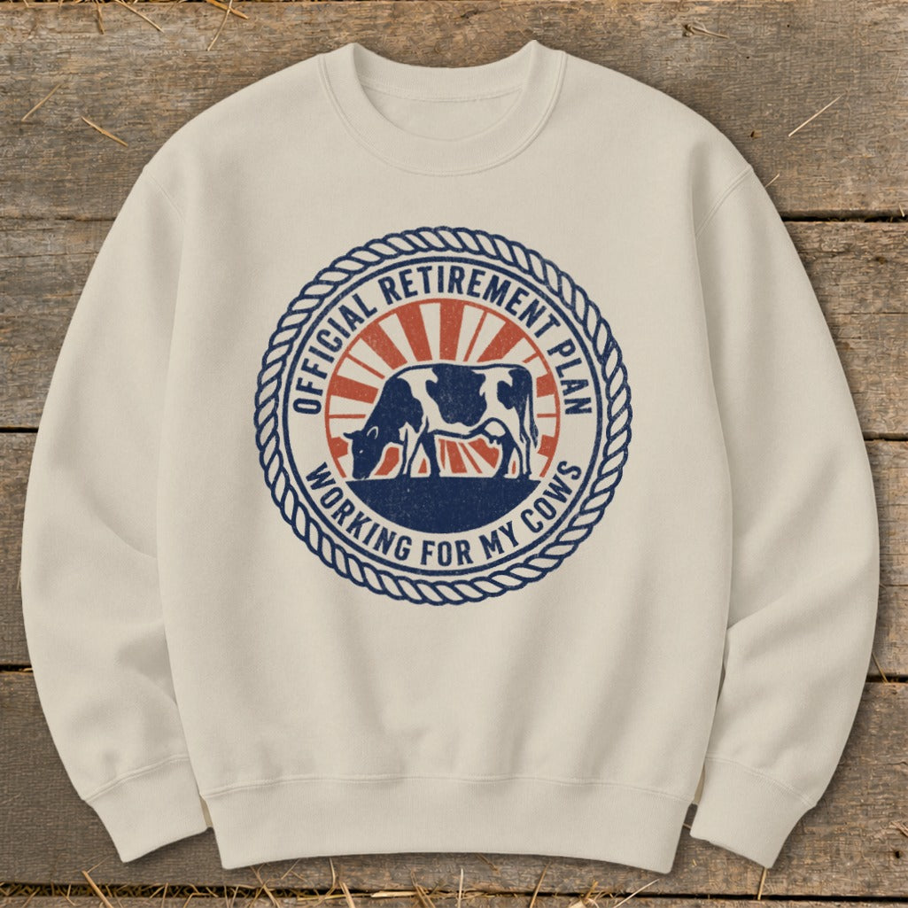 Cream sweatshirt with circular graphic: cow, sunburst, "Official Retirement Plan Working For My Cows".