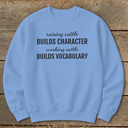 Light blue sweatshirt with black text "raising cattle BUILDS CHARACTER working cattle BUILDS VOCABULARY".