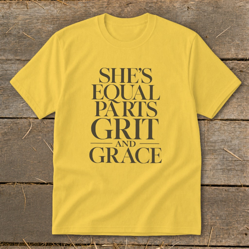 Yellow t-shirt with dark grey text reading "SHE'S EQUAL PARTS GRIT AND GRACE".