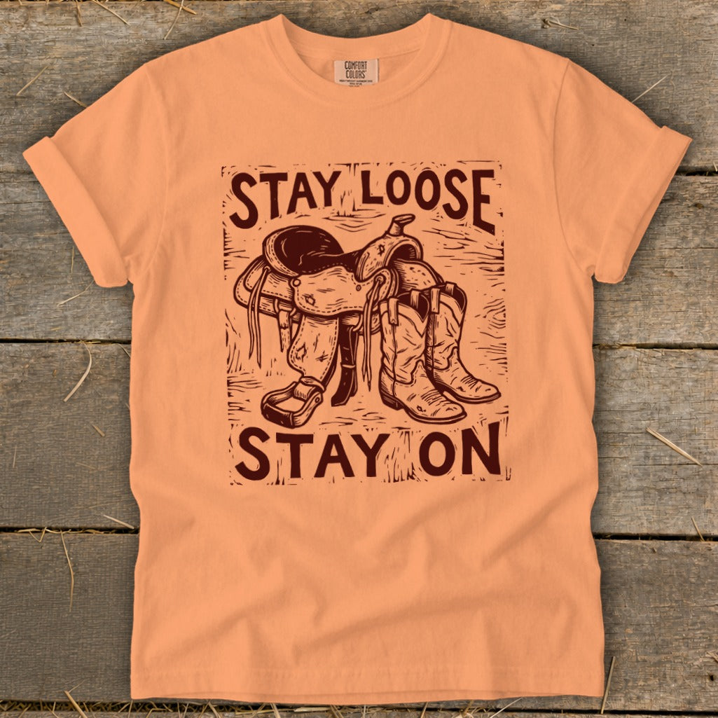 Peach t-shirt with "STAY LOOSE STAY ON" text and saddle and boots graphic.