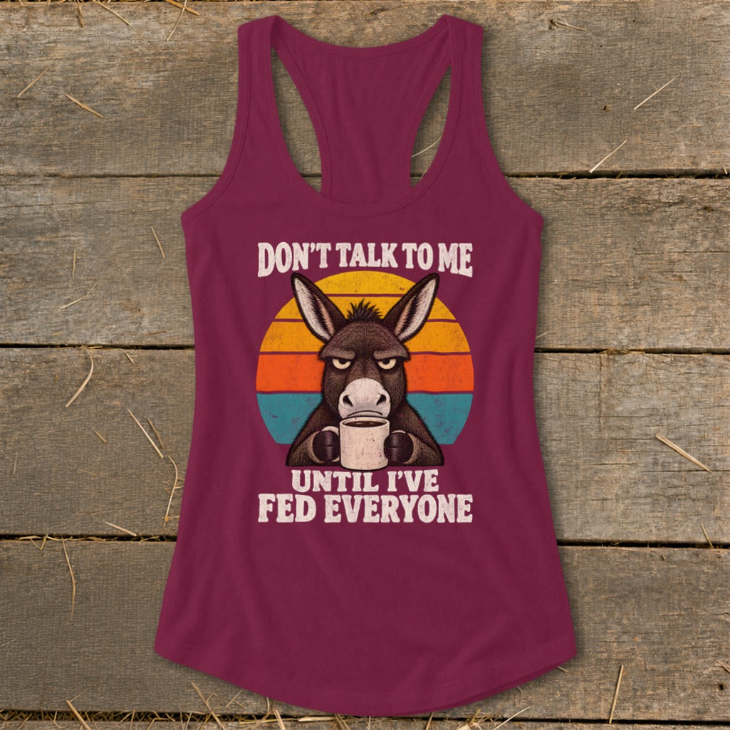 Maroon racerback tank top featuring a graphic of a grumpy donkey holding a coffee mug with the text Don't Talk to Me Until I've Fed Everyone.