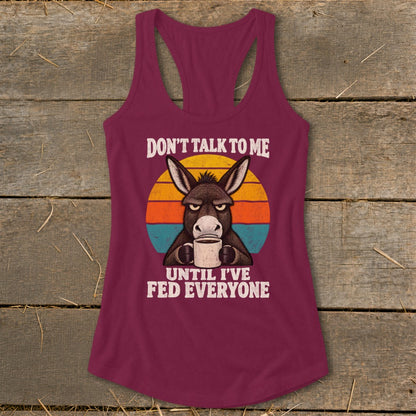 Maroon racerback tank top featuring a graphic of a grumpy donkey holding a coffee mug with the text Don't Talk to Me Until I've Fed Everyone.