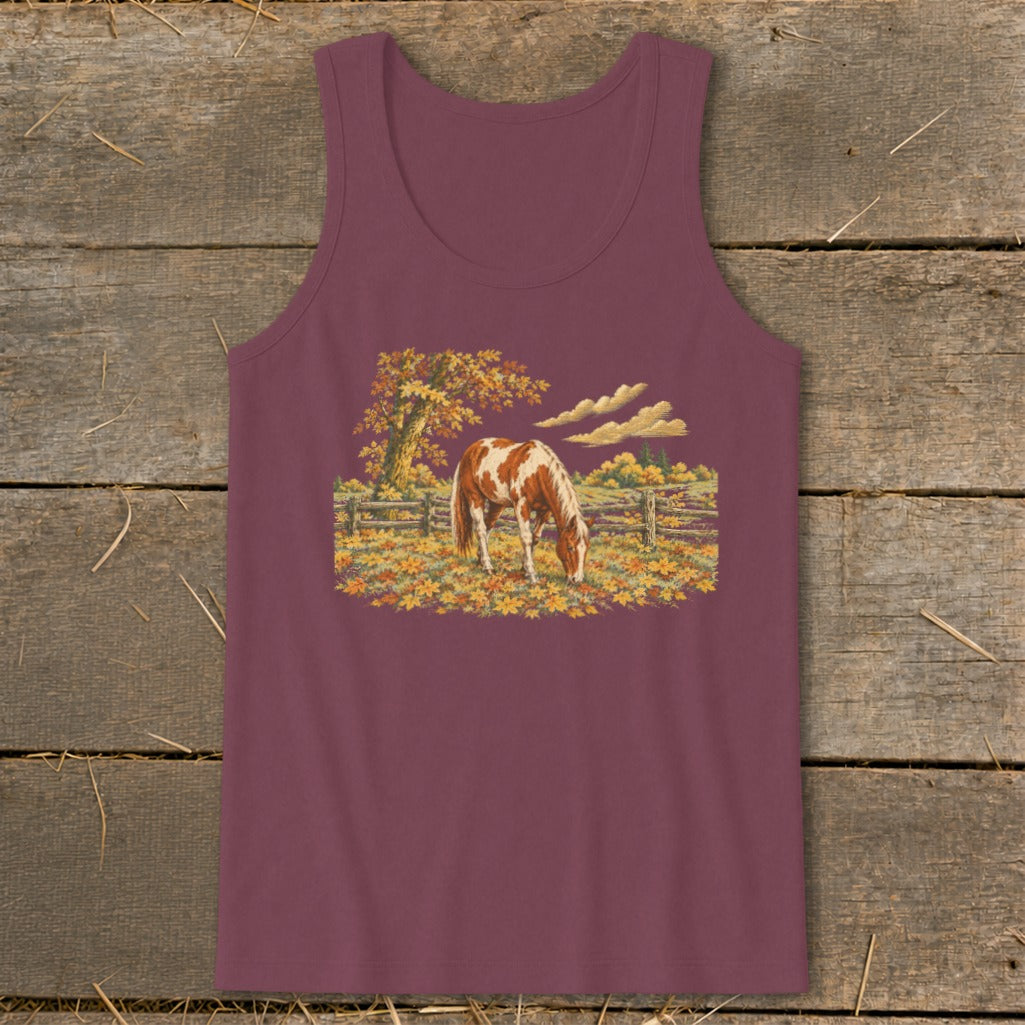 Brown and white horse grazing in an autumn field with fallen leaves and trees.