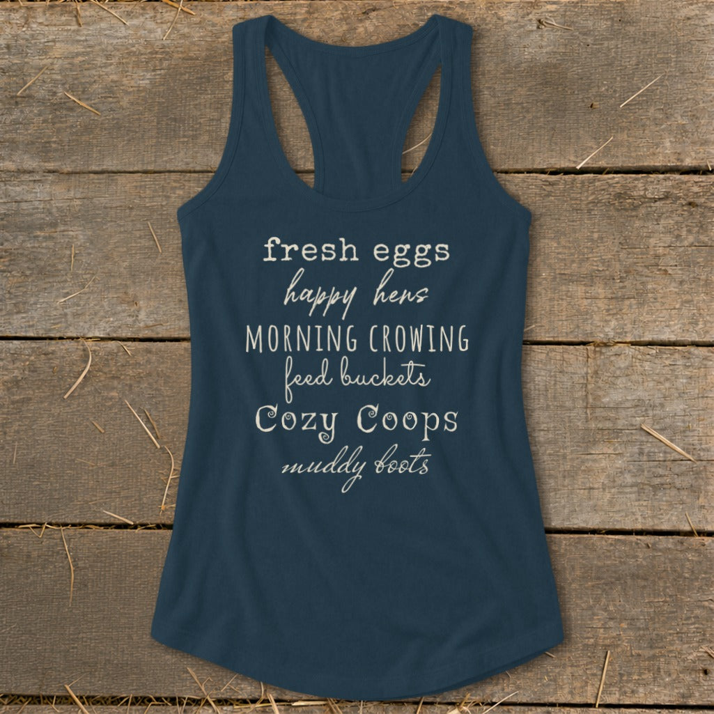 Blue tank top with white text: fresh eggs, happy hens, morning crowing, feed buckets, cozy coops, muddy boots.