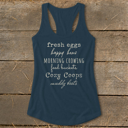 Blue tank top with white text: fresh eggs, happy hens, morning crowing, feed buckets, cozy coops, muddy boots.