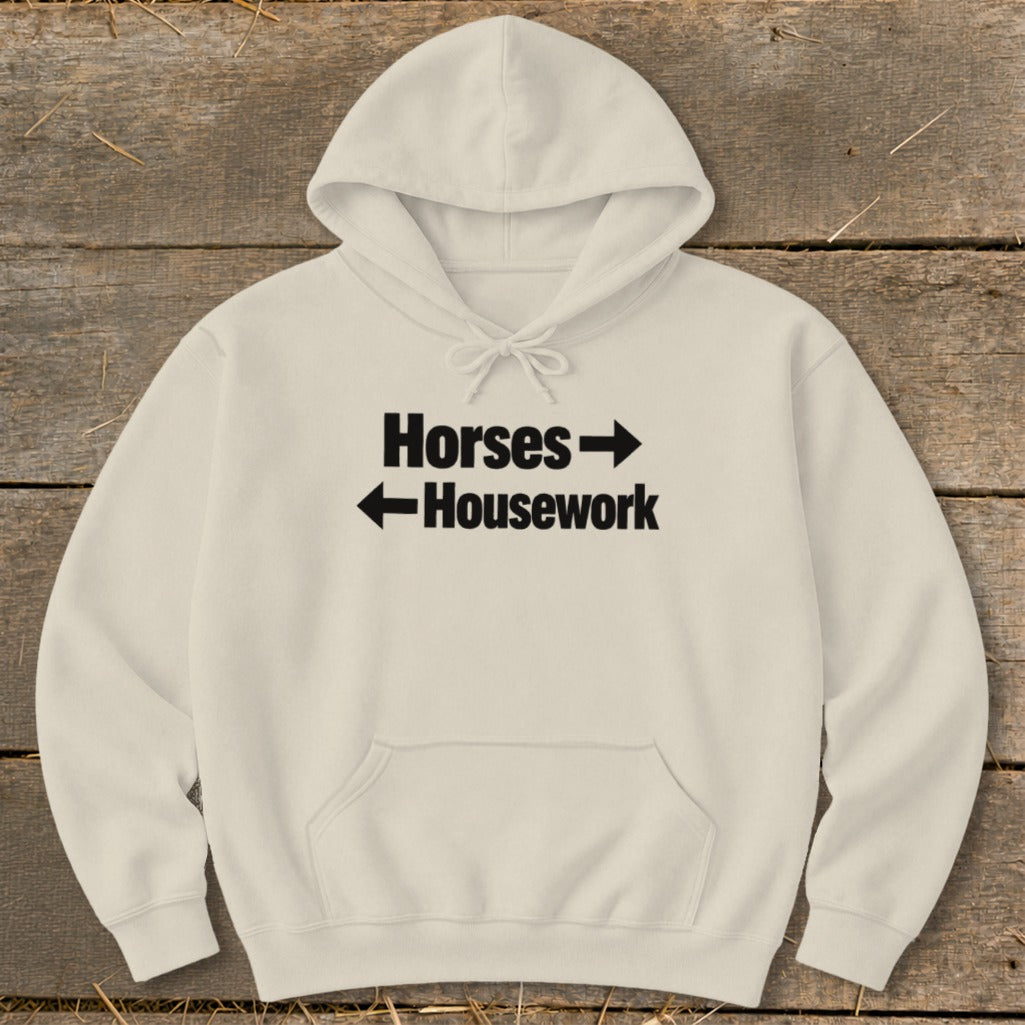 A cream-colored hoodie features black text that reads Horses with a right arrow above Housework with a left arrow.