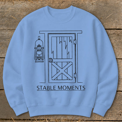 Light blue sweatshirt with a line drawing of a barn door and hanging lantern. Text reads "STABLE MOMENTS."