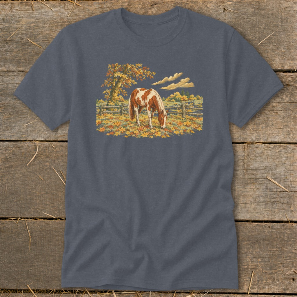 Brown and white horse grazing in a field of autumn leaves with a fence and tree.