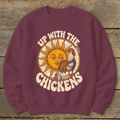 Maroon crewneck sweatshirt featuring a graphic of a rooster, a smiling sun, and text reading Up With the Chickens.