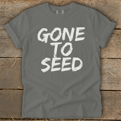 Gray t-shirt with white text "GONE TO SEED" on a wooden background.