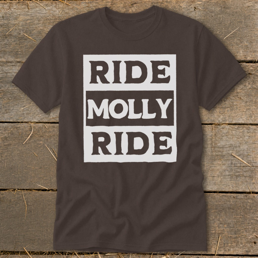 Brown short-sleeve t-shirt with a white graphic containing the text Ride Molly Ride laid on a rustic wooden background.