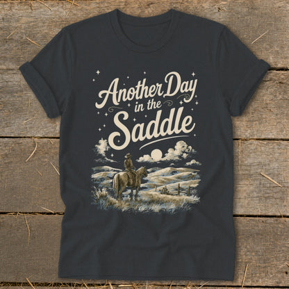 T-shirt graphic with text "Another Day in the Saddle" and a cowboy on horseback.