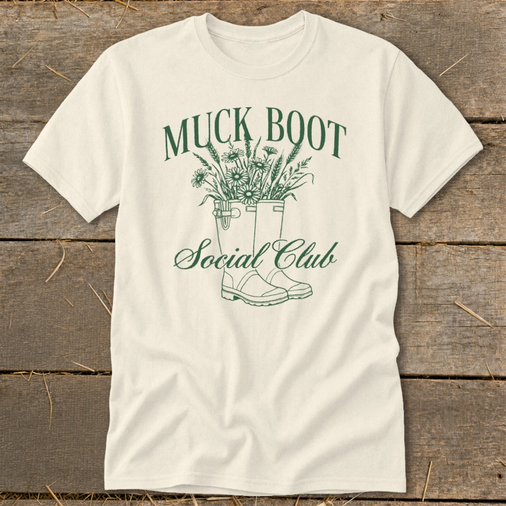 Cream t-shirt with green text and illustration of muck boots filled with flowers.