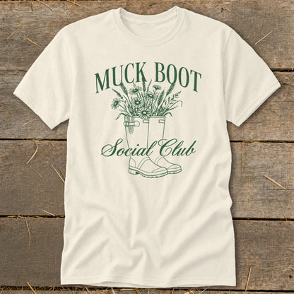 Cream t-shirt with green text and illustration of muck boots filled with flowers.