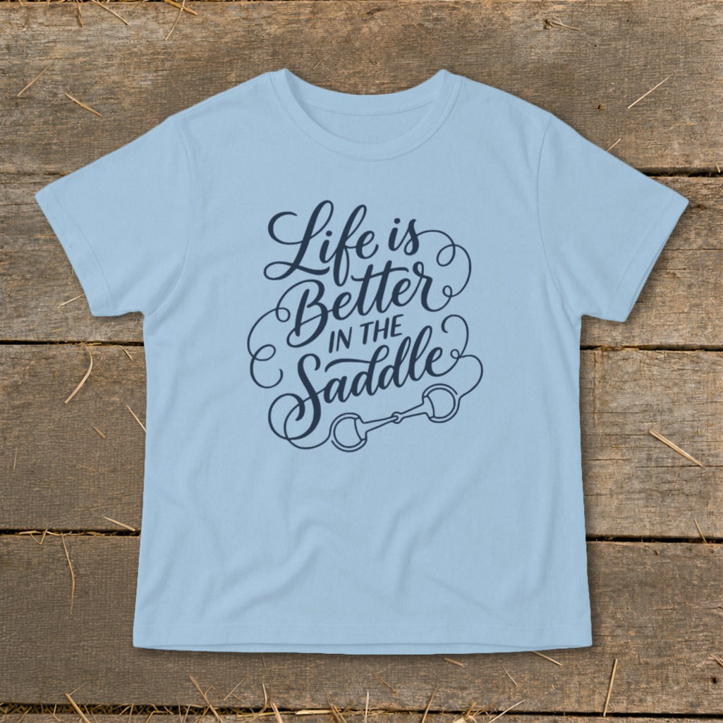 Light blue t-shirt with navy blue text reading "Life is Better In The Saddle" and a horse bit graphic.