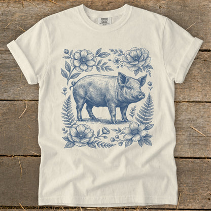 Pig illustration surrounded by blue floral and fern border on a cream t-shirt.