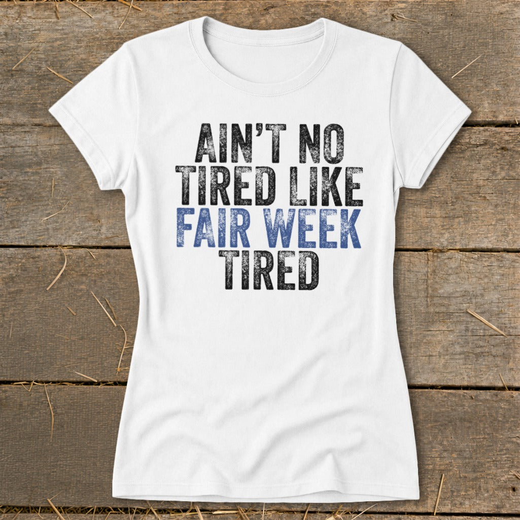 White t-shirt with distressed text that reads "AIN'T NO TIRED LIKE FAIR WEEK TIRED".