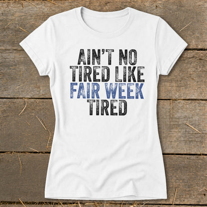 White t-shirt with distressed text that reads "AIN'T NO TIRED LIKE FAIR WEEK TIRED".