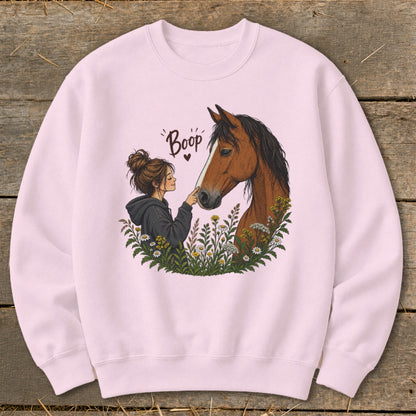 Pink sweatshirt with illustration of girl booping a horse's nose, surrounded by flowers.