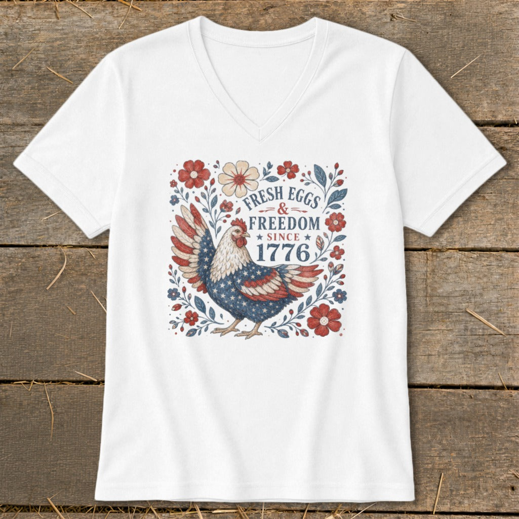 White v-neck t-shirt with a patriotic chicken graphic and text "Fresh Eggs & Freedom Since 1776".