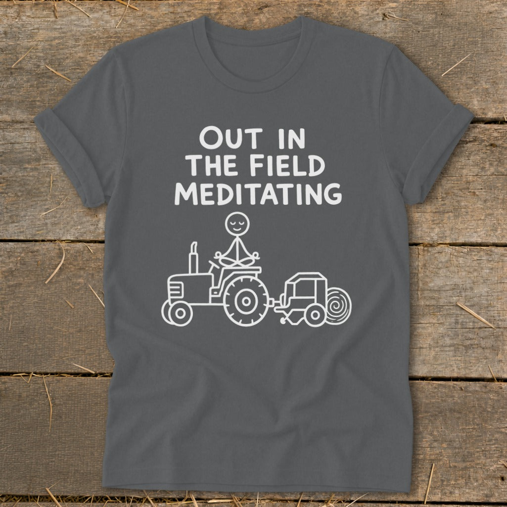 Grey t-shirt with white text "OUT IN THE FIELD MEDITATING" and a stick figure meditating on a tractor.