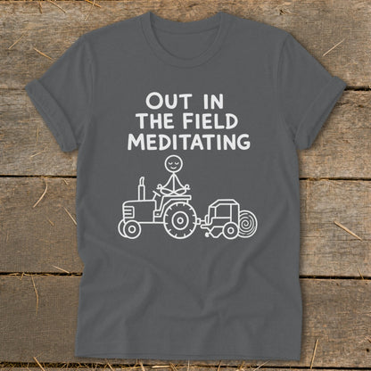 Grey t-shirt with white text "OUT IN THE FIELD MEDITATING" and a stick figure meditating on a tractor.