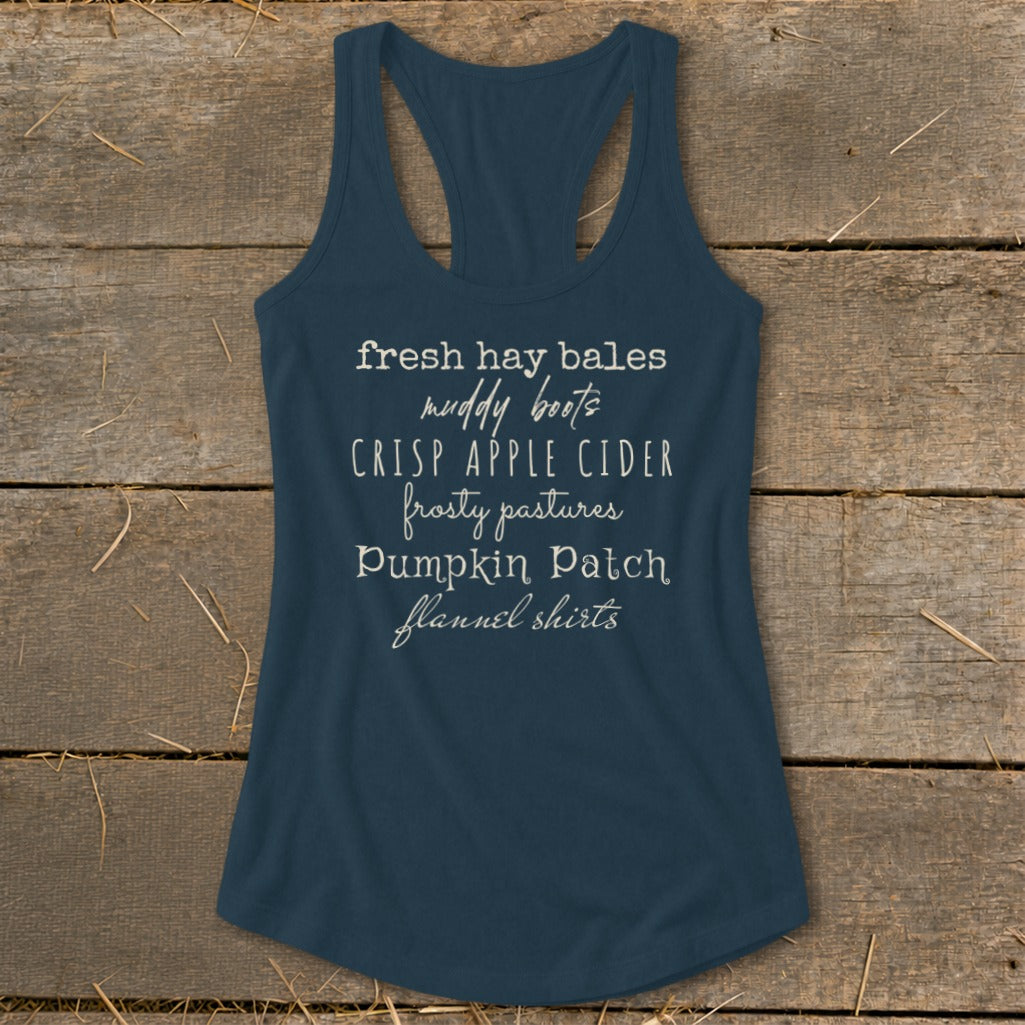 Navy tank top with white text listing fall activities: fresh hay bales, muddy boots, crisp apple cider, frosty pastures, pumpkin patch, flannel shirts.