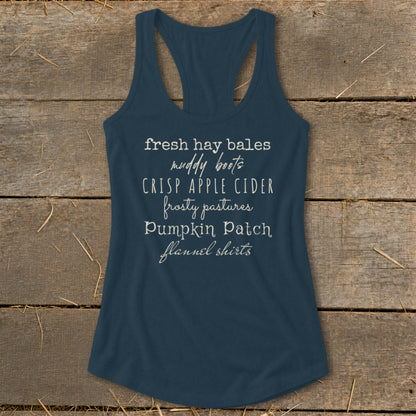 Navy tank top with white text listing fall activities: fresh hay bales, muddy boots, crisp apple cider, frosty pastures, pumpkin patch, flannel shirts.