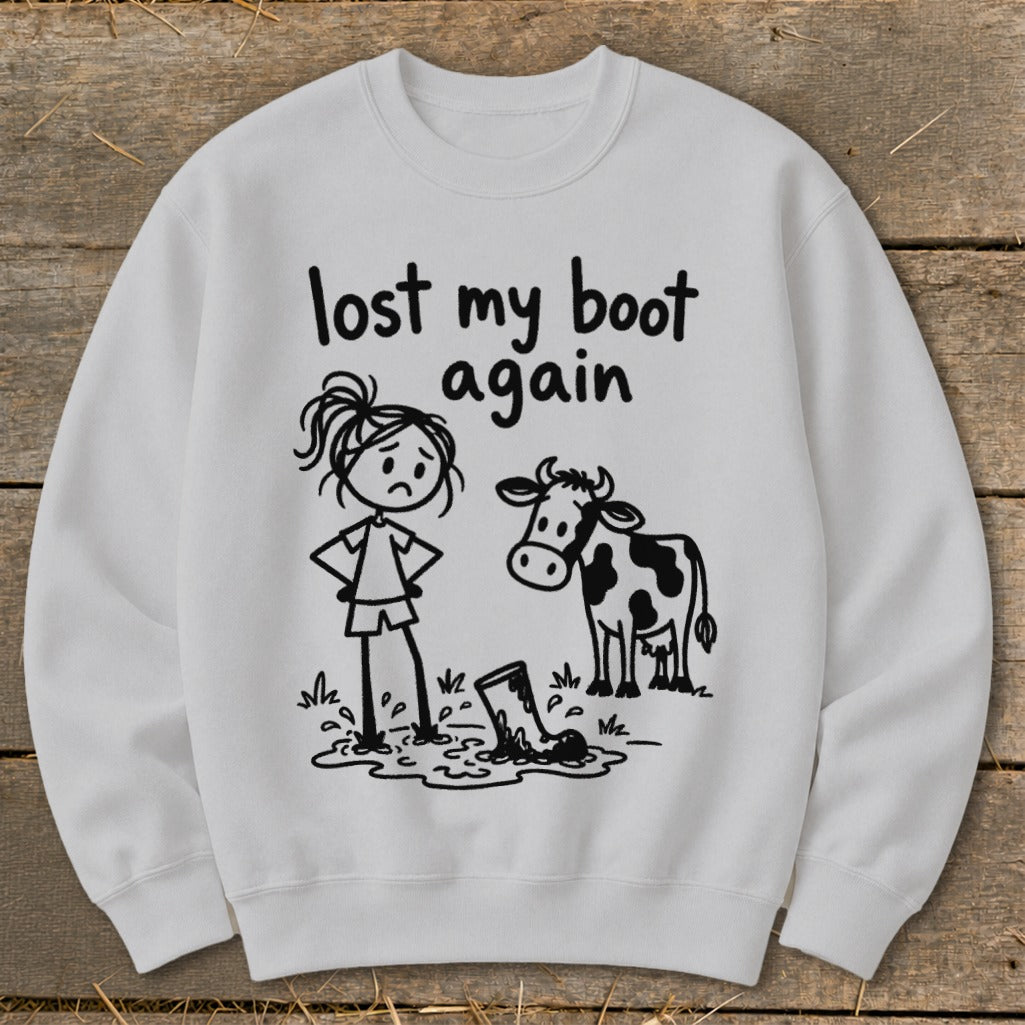 Light gray crewneck sweatshirt featuring a graphic of a sad stick-figure girl, a cow, and a lost boot in mud with the text lost my boot again.