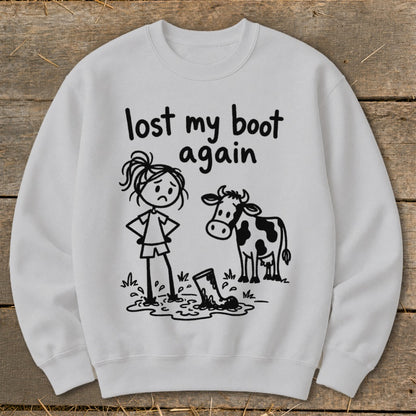 Light gray crewneck sweatshirt featuring a graphic of a sad stick-figure girl, a cow, and a lost boot in mud with the text lost my boot again.
