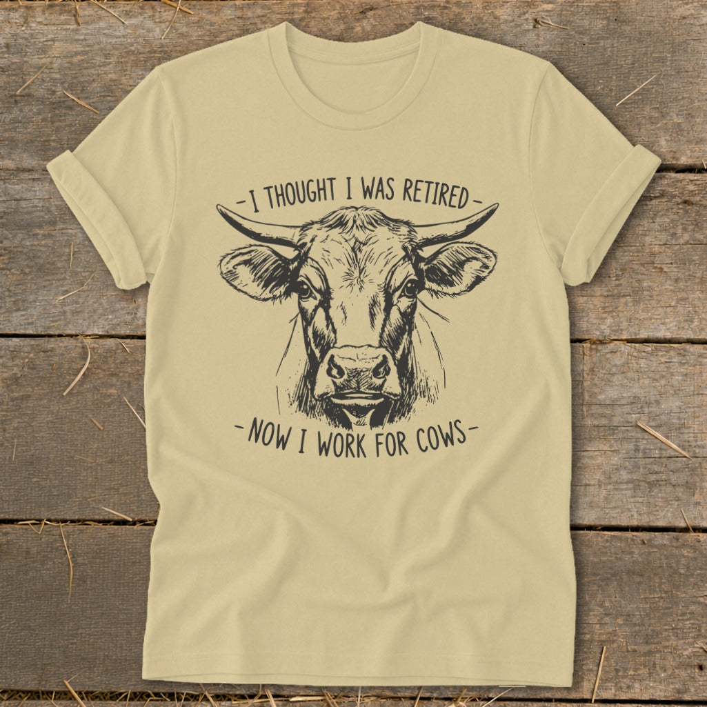 Light yellow t-shirt with black sketch of cow's head and text "I thought I was retired - Now I work for cows".