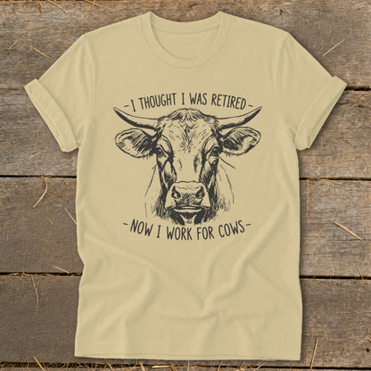 Light yellow t-shirt with black sketch of cow's head and text "I thought I was retired - Now I work for cows".
