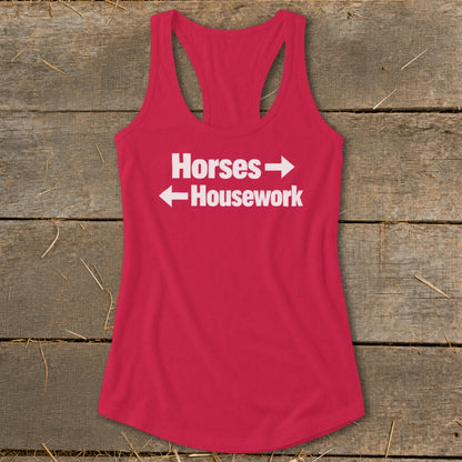 A red women's racerback tank top with white text that reads Horses with a right arrow and Housework with a left arrow, displayed on a rustic wooden background.