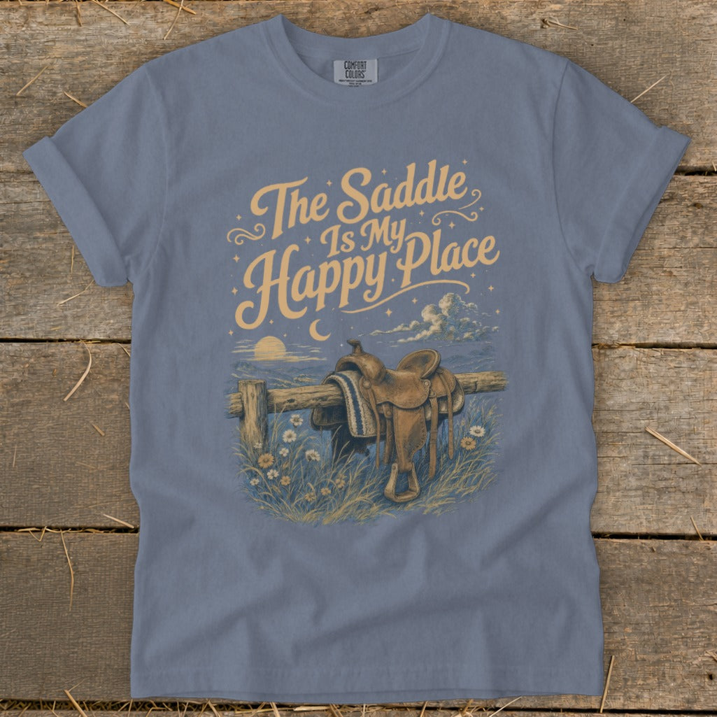 T-shirt graphic with text "The Saddle Is My Happy Place" over a saddle on a fence.