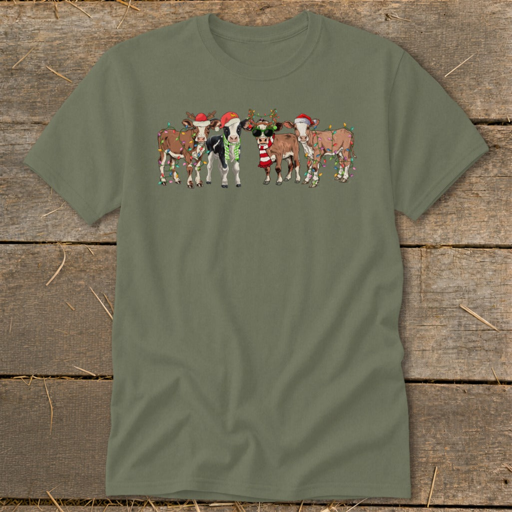 Five cartoon cows wear Santa hats and Christmas lights on a green t-shirt.
