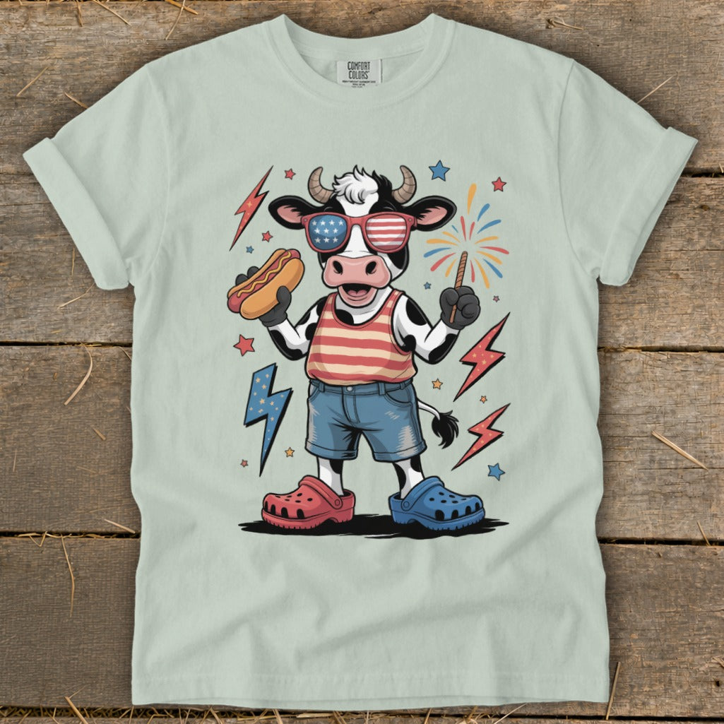 Cartoon cow wearing sunglasses and holding a hot dog, celebrating Fourth of July.