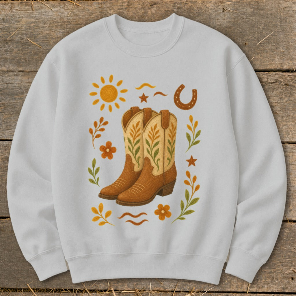 White sweatshirt with graphic of cowboy boots, sun, horseshoe, stars, and flowers.