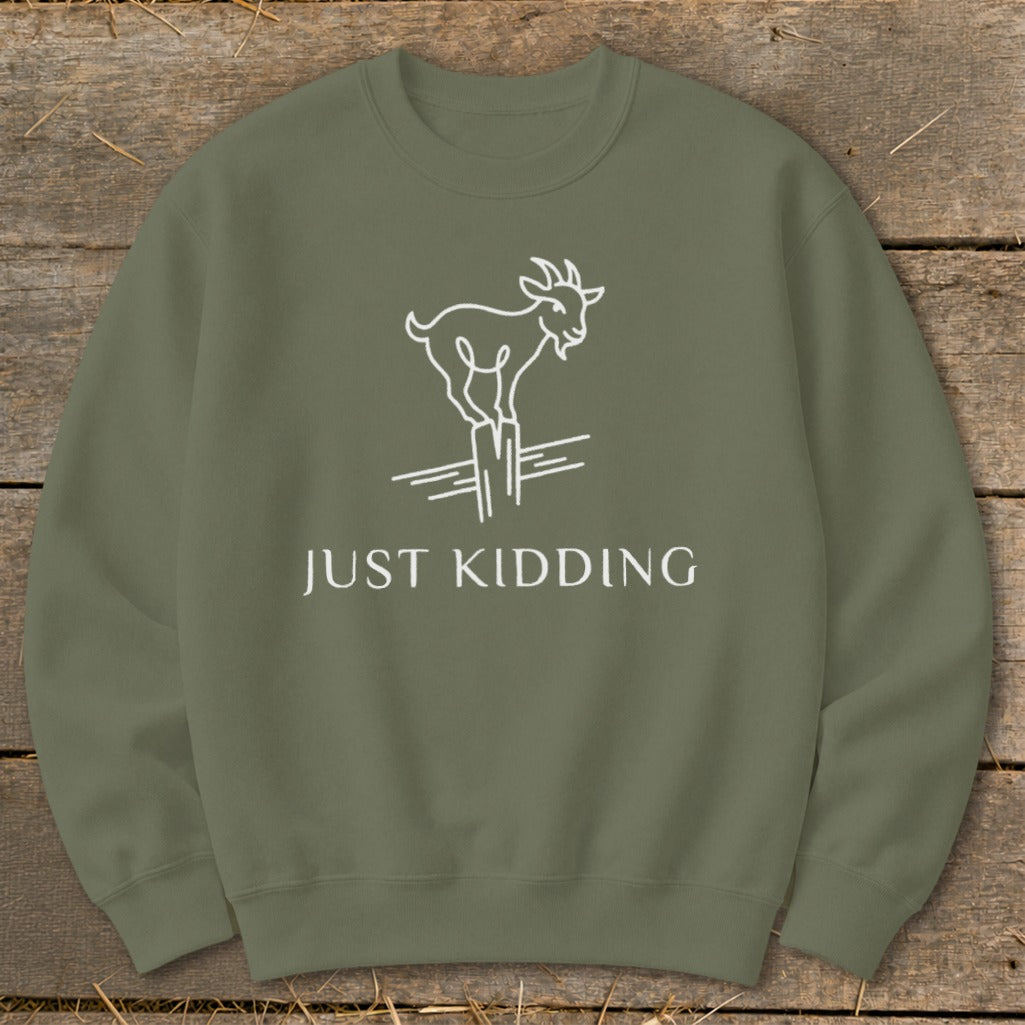 Olive green sweatshirt with white line art of a goat on a post and text "JUST KIDDING".