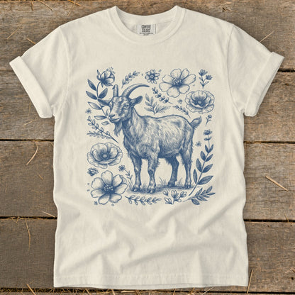 White t-shirt with a blue ink sketch of a goat surrounded by flowers and leaves.