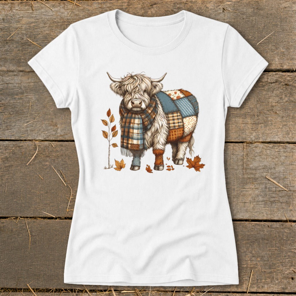 White t-shirt with a Highland cow illustration wearing a plaid scarf and patchwork coat.