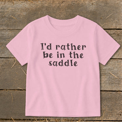Pink t-shirt with black text that says "I'd rather be in the saddle".