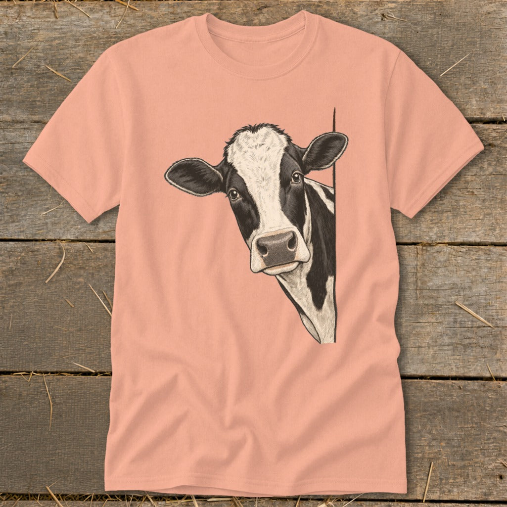 Black and white cow peeking from the side on a peachy t-shirt.