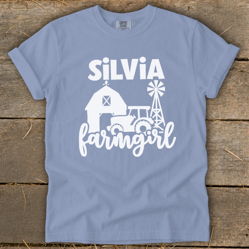 Light blue t-shirt with white graphic of barn, tractor, windmill, and "Silvia farmgirl".