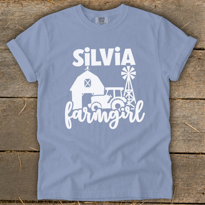 Light blue t-shirt with white graphic of barn, tractor, windmill, and "Silvia farmgirl".