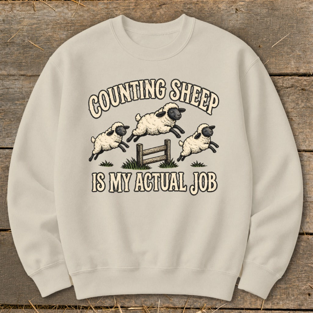 Cream sweatshirt with "Counting Sheep Is My Actual Job" text and jumping sheep graphic.