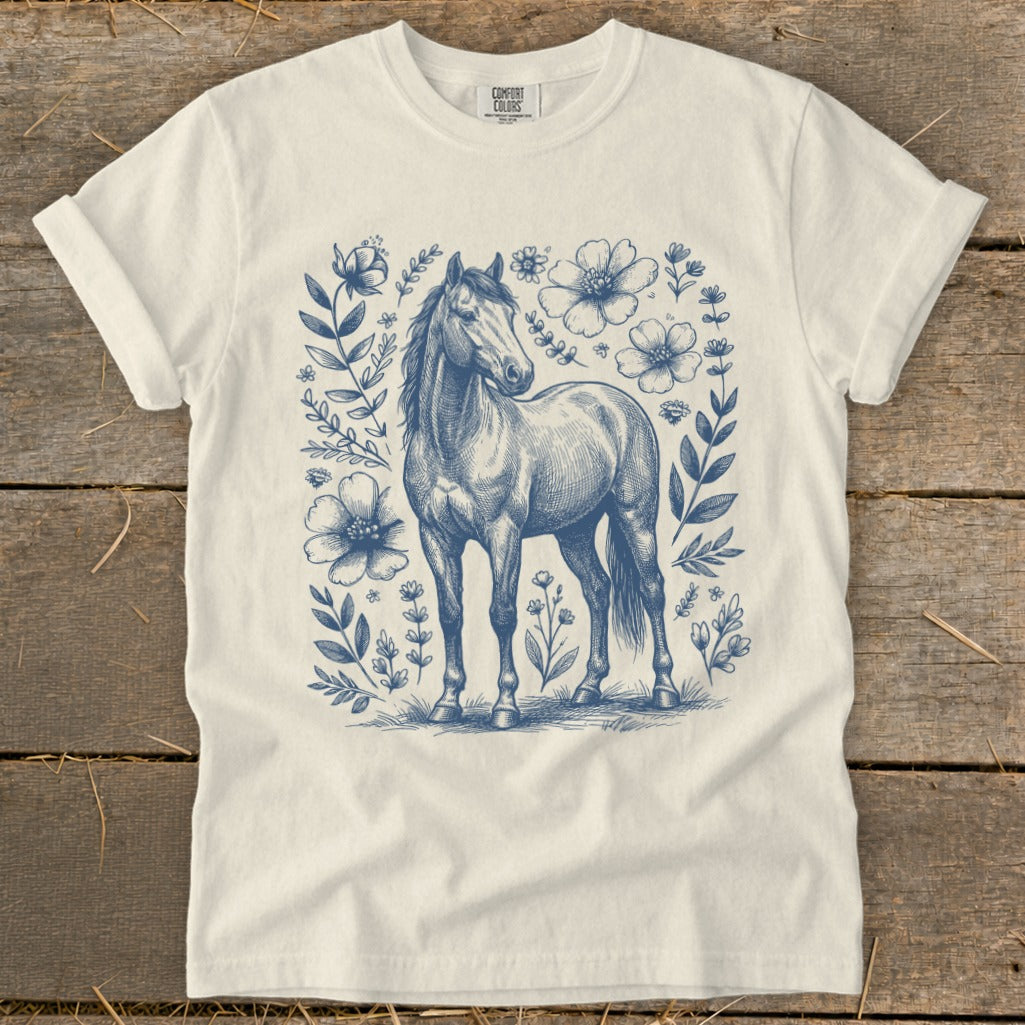 Cream t-shirt with blue line art of a horse surrounded by flowers and foliage.