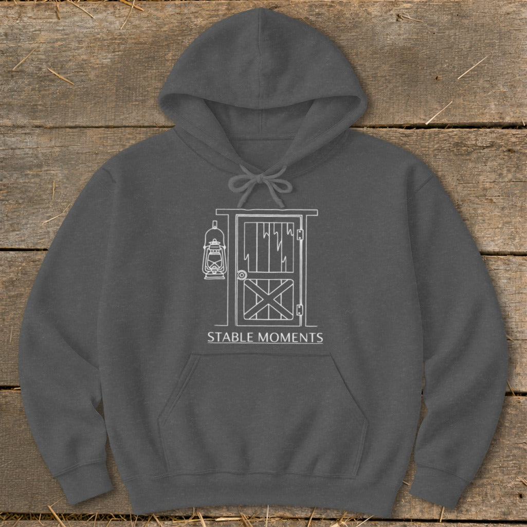 Charcoal hoodie with white line art of a barn door and lantern. Text reads "STABLE MOMENTS".
